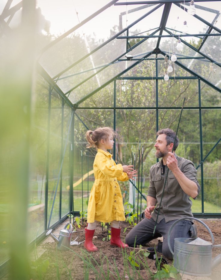 Father and daughter in a yellow dress and red rubber boots working together in a green house