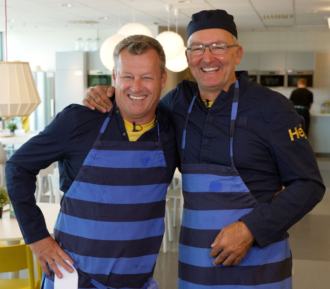 Jesper Brodin and Juvencio Maeztu wearing aprons standing in a IKEA stores co-worker cantina smiling.