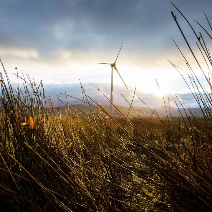 A windturbine on a large field with mountains in the background.