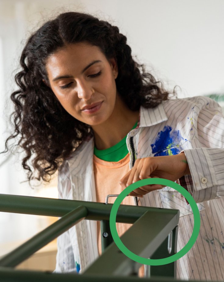 A person wearing a paint-stained shirt is painting a chair green with a roller.