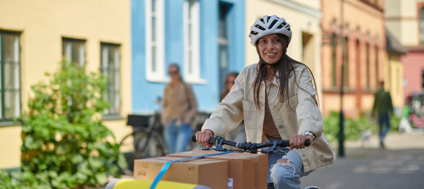 A woman wearing a helmet rides a cargo bike loaded with IKEA packages on a cozy city street.