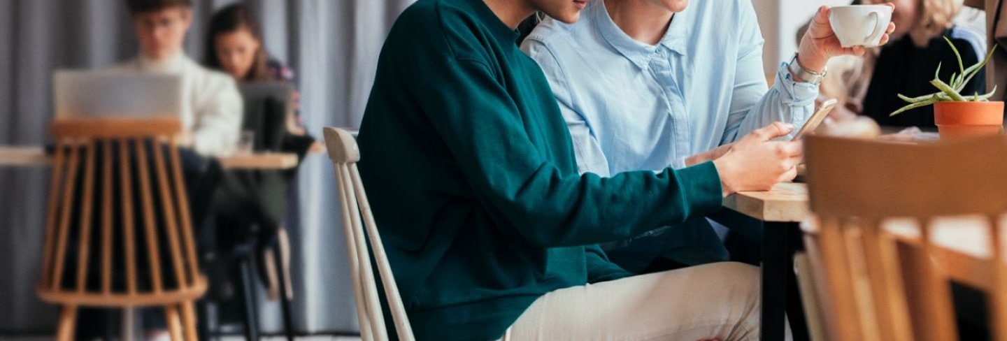 Two friends sitting in a café browsing on a phone