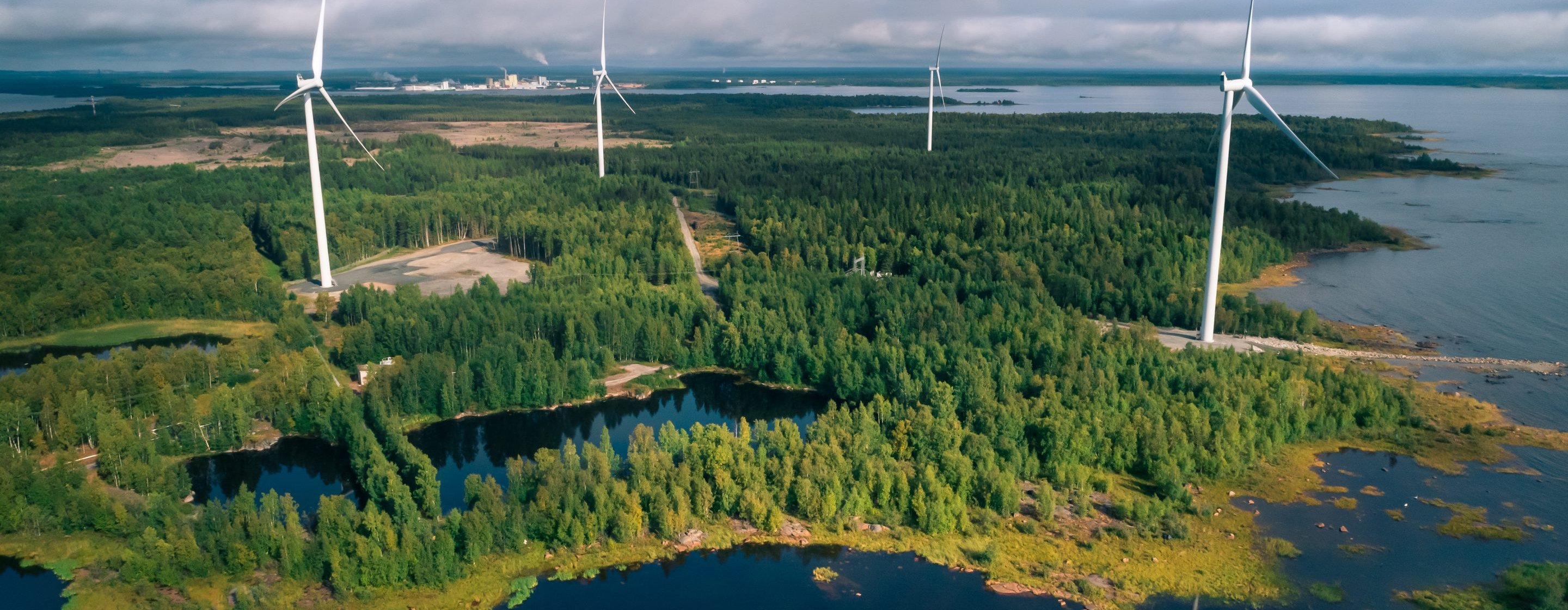 View over a windfarm in a forest by a shore in Finland.