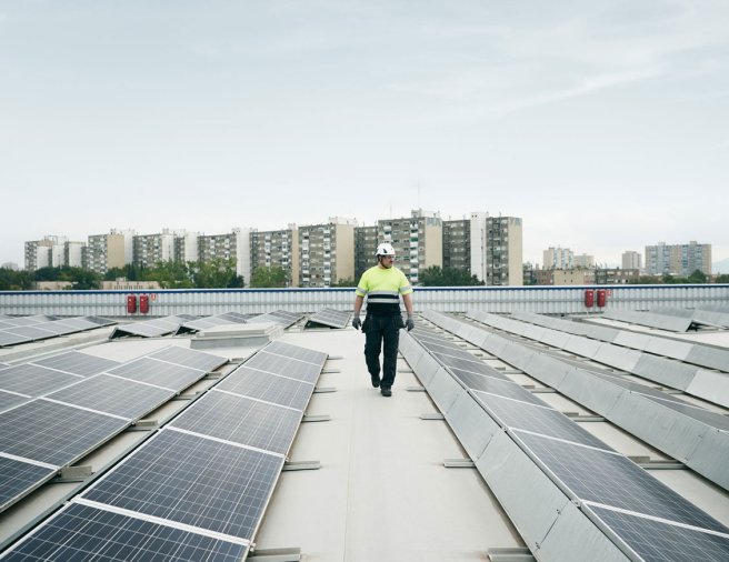 Man walking on a roof top with solar panels, high rise buildings in the background