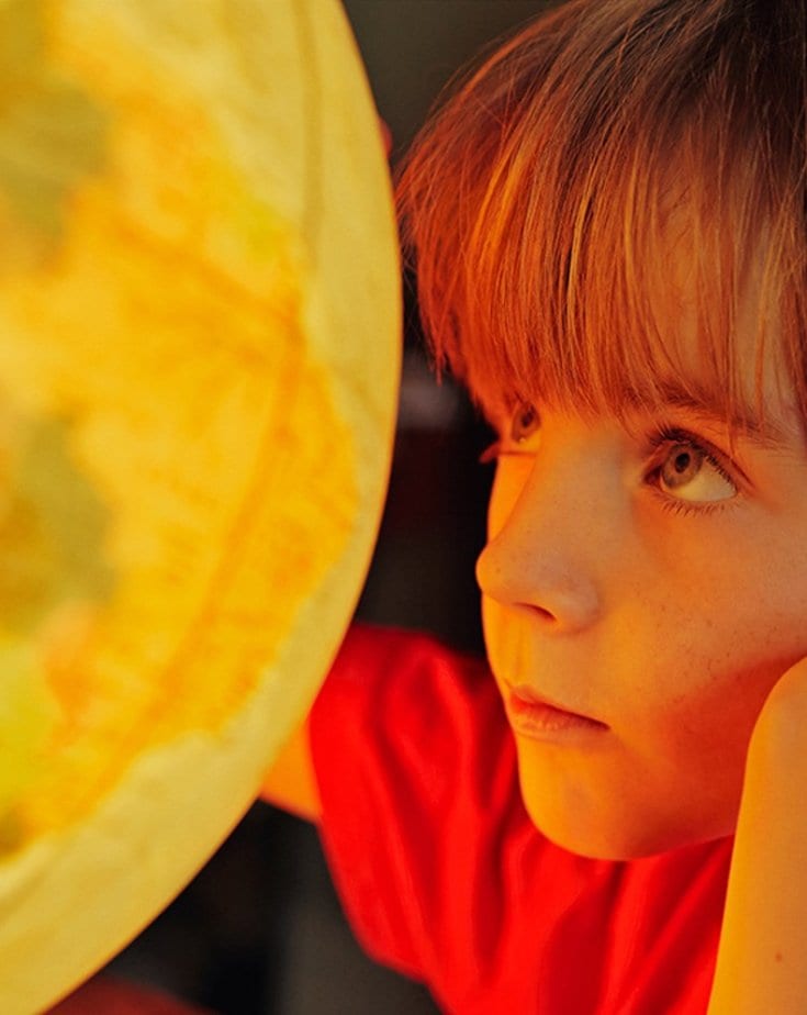 A child with a red t-shirt looking closely into a lit globe.