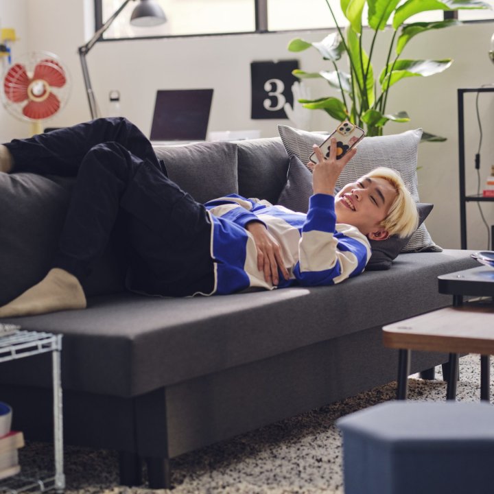 A person laying in a sofa looking into a smartphone and smiling.