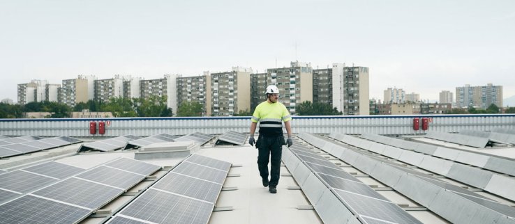 Man walking on a roof top with solar panels, high rise buildings in the background