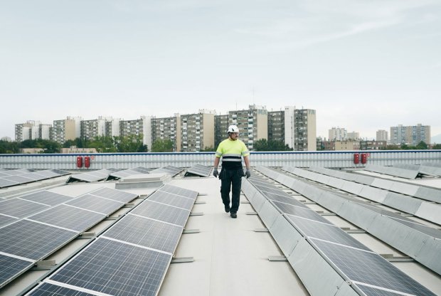 Man walking on a roof top with solar panels, high rise buildings in the background